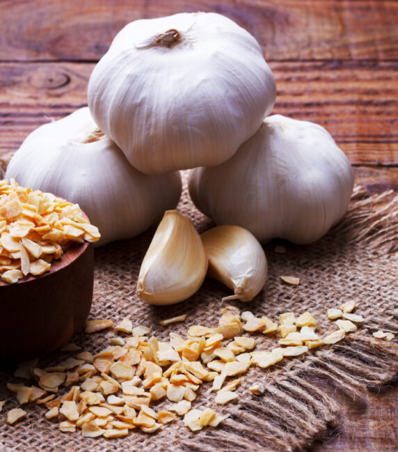 garlic cloves, bulb and flakes on old wooden board