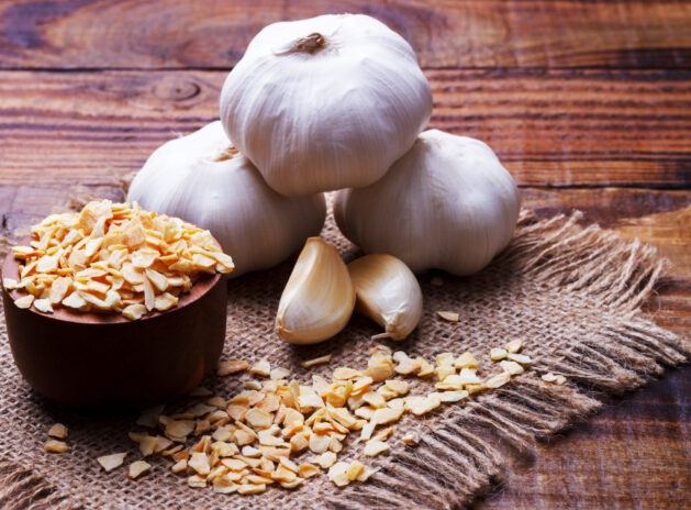 garlic cloves, bulb and flakes on old wooden board