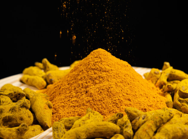 Turmeric powder and dried turmeric root on a black background.