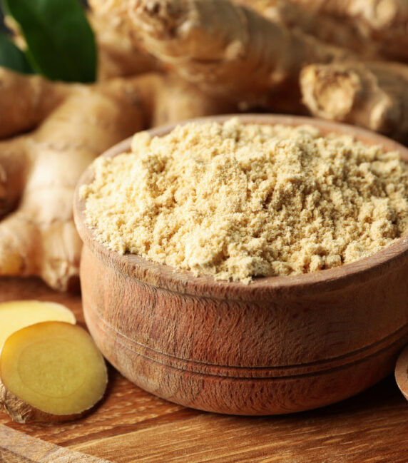 Board with ginger and ginger powder on wooden background