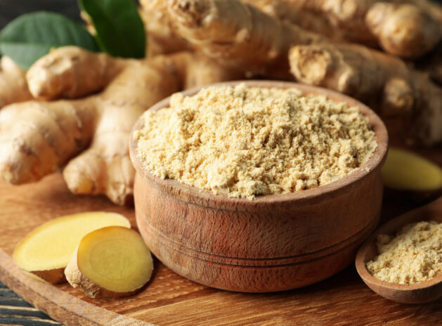 Board with ginger and ginger powder on wooden background